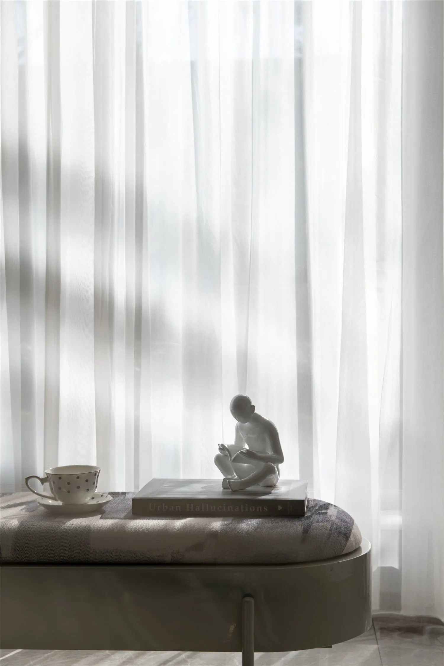 A serene interior space featuring a fabric curtain, a ceramic statue, a book, and a teacup with a saucer.
