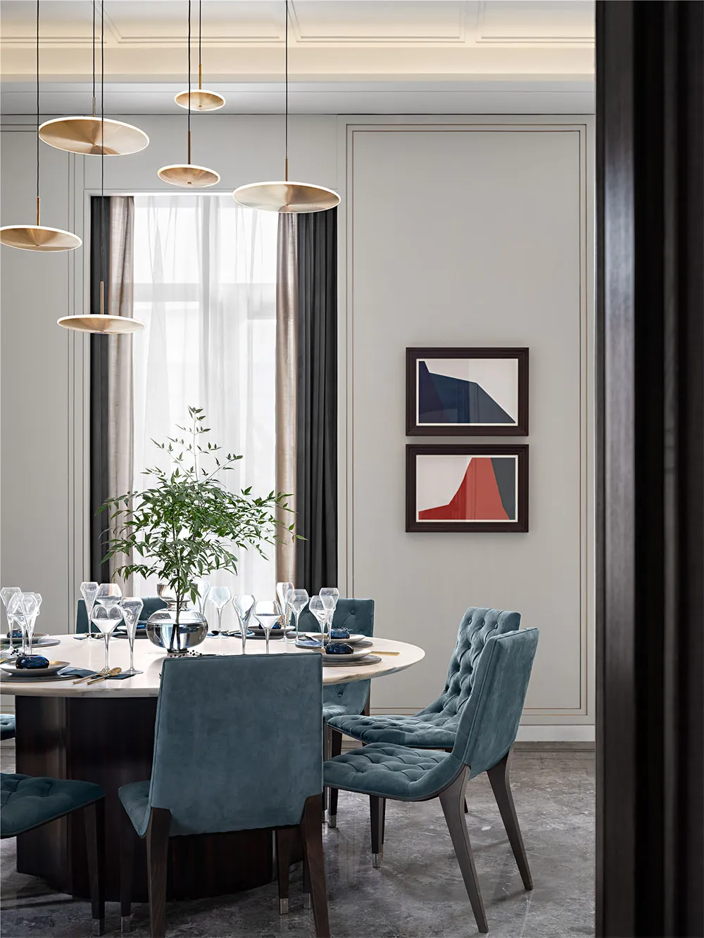 Modern dining room with a round table, blue upholstered chairs, marble top, and hanging pendant lights.