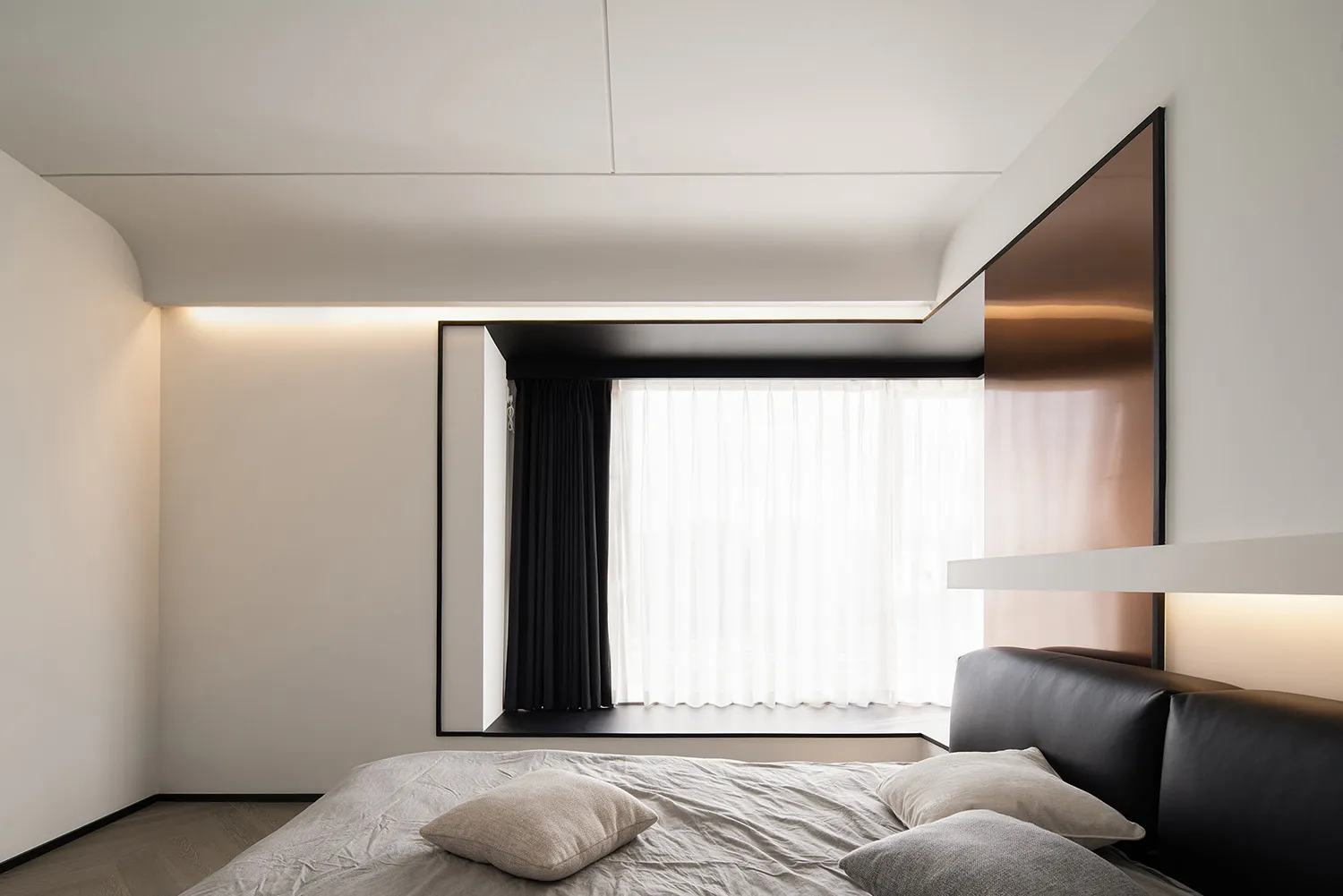 A minimalist bedroom with a metallic headboard, white curtains, and brown laminate flooring.
