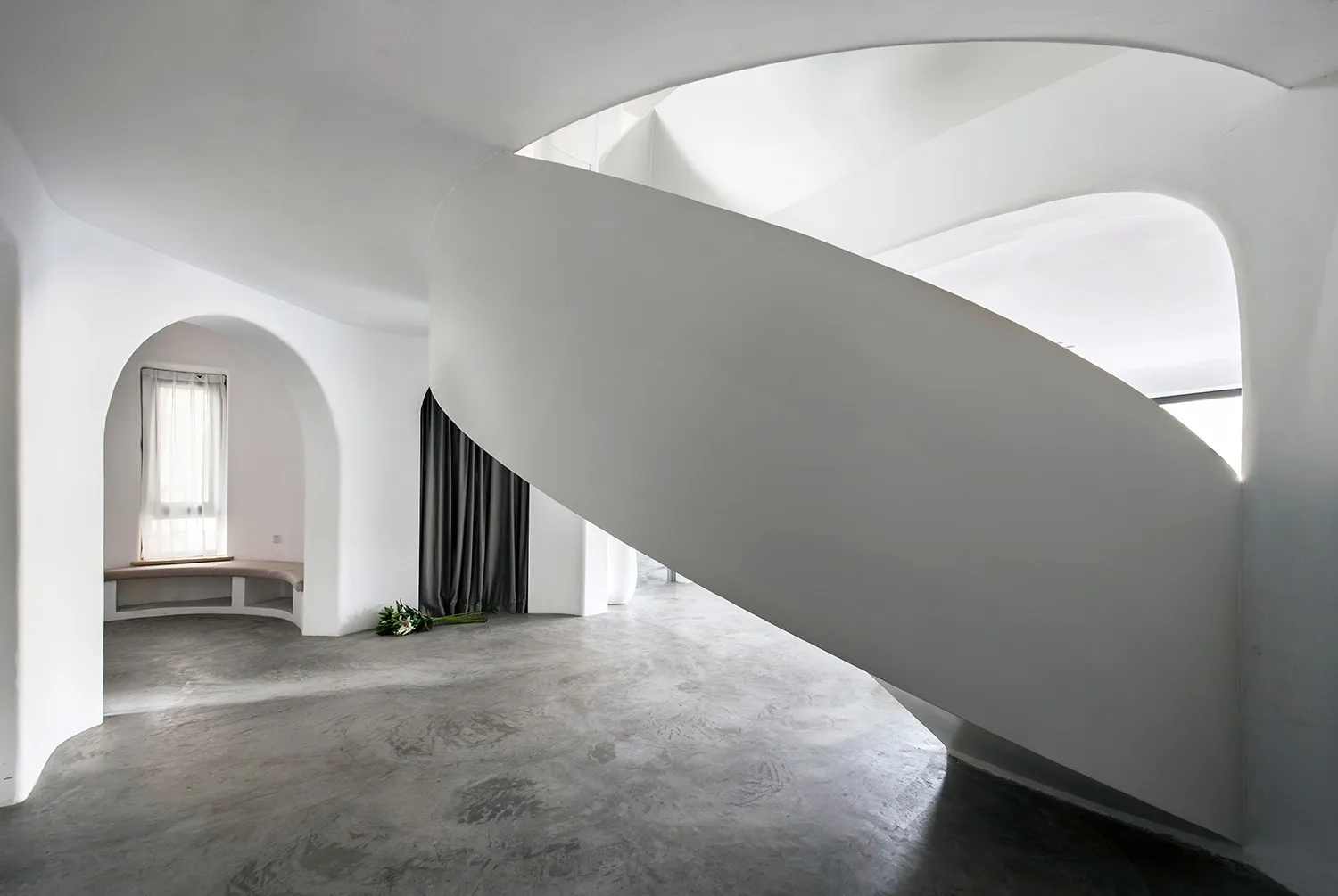 A modern, minimalist interior with concrete walls and spiral staircase.