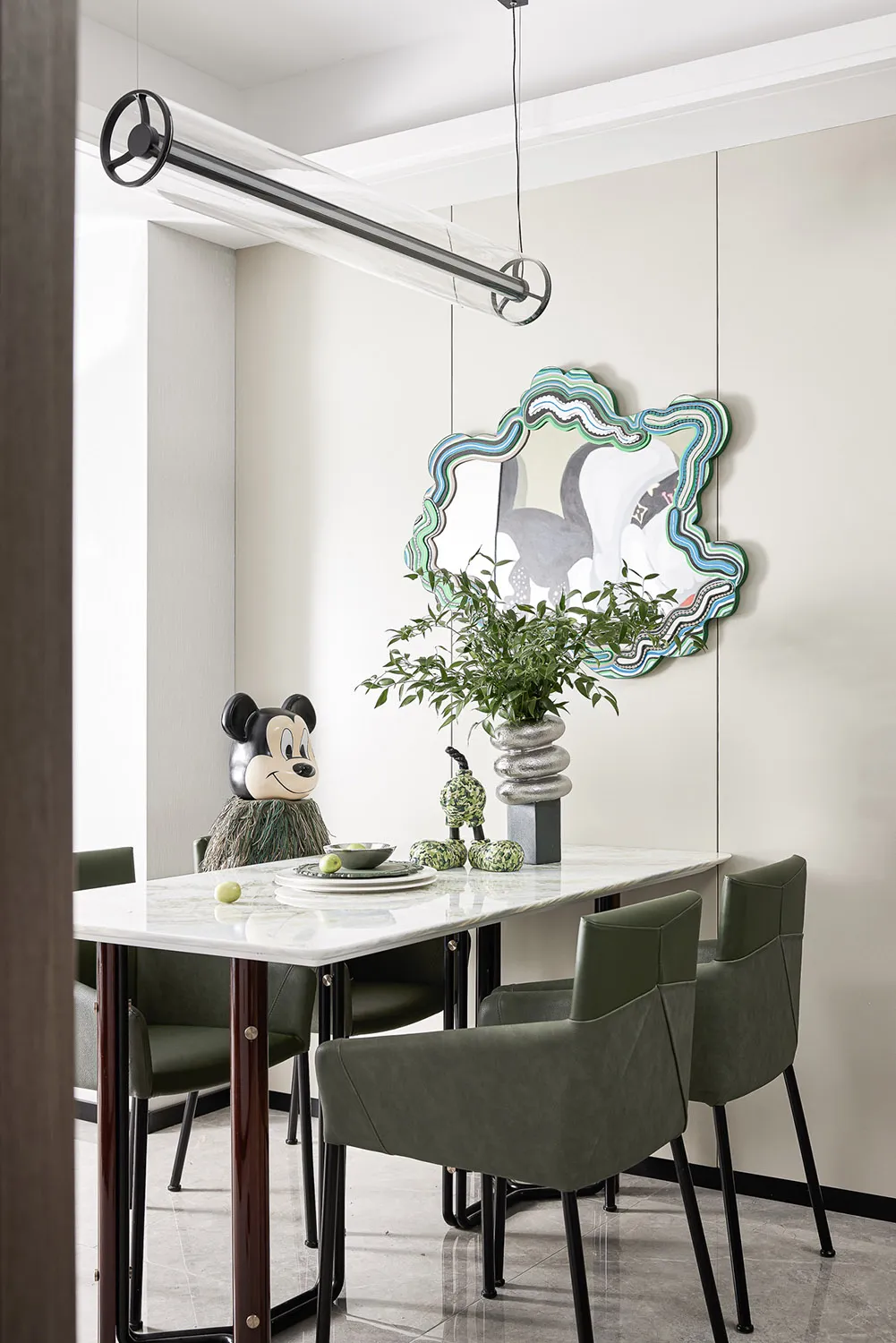 A modern dining room with a marble table, green leather chairs, and a decorative mirror.