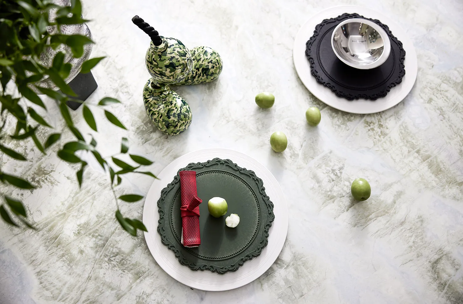 Modern green ceramic dinnerware with red napkins and green apples on a light, textured table surface.
