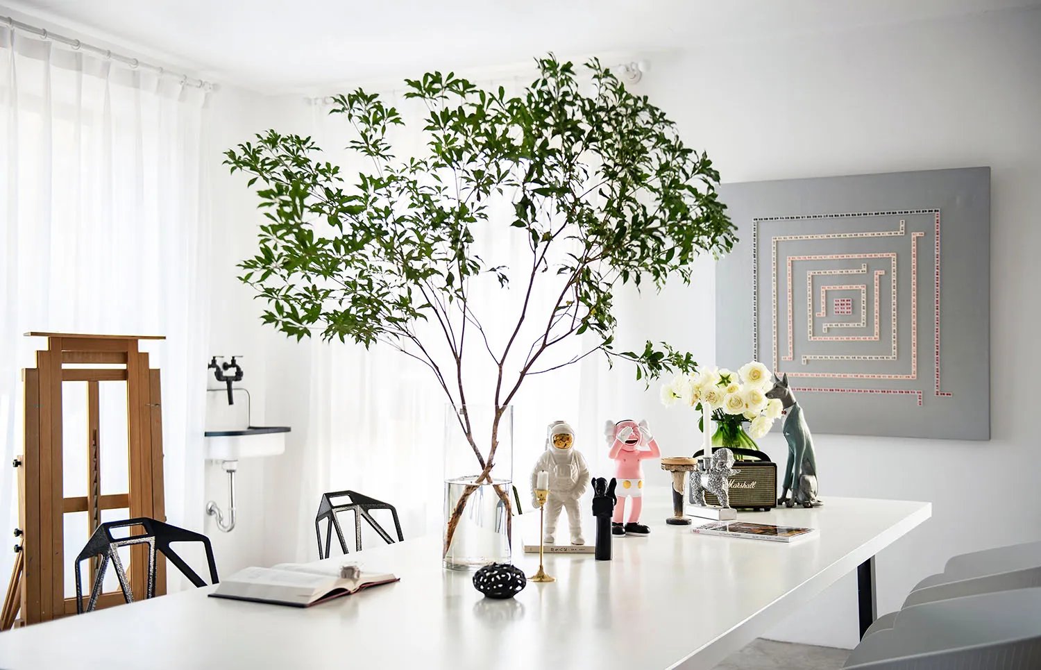 A modern living room with white furniture, a large green plant, and decorative objects on a table.