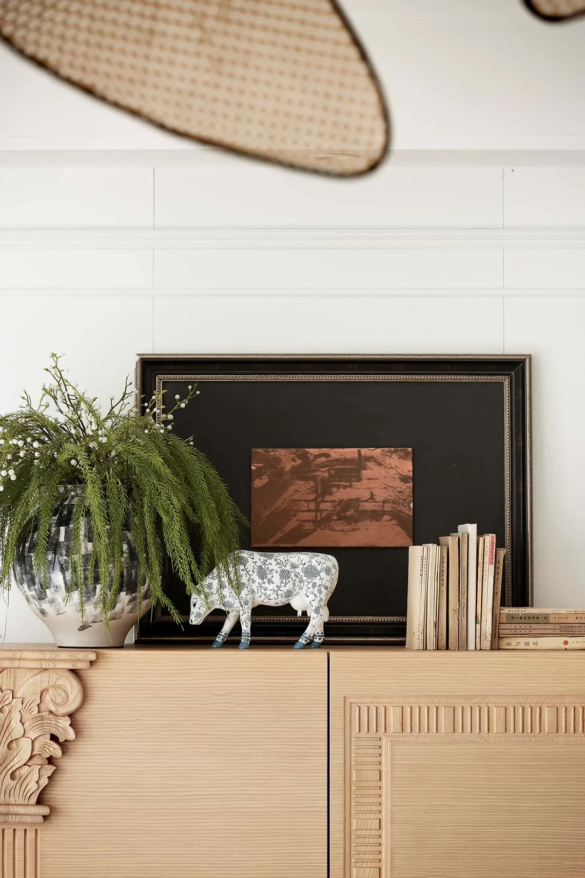 A modern interior space featuring a wooden cabinet topped with a plant, statue, books, and framed picture.