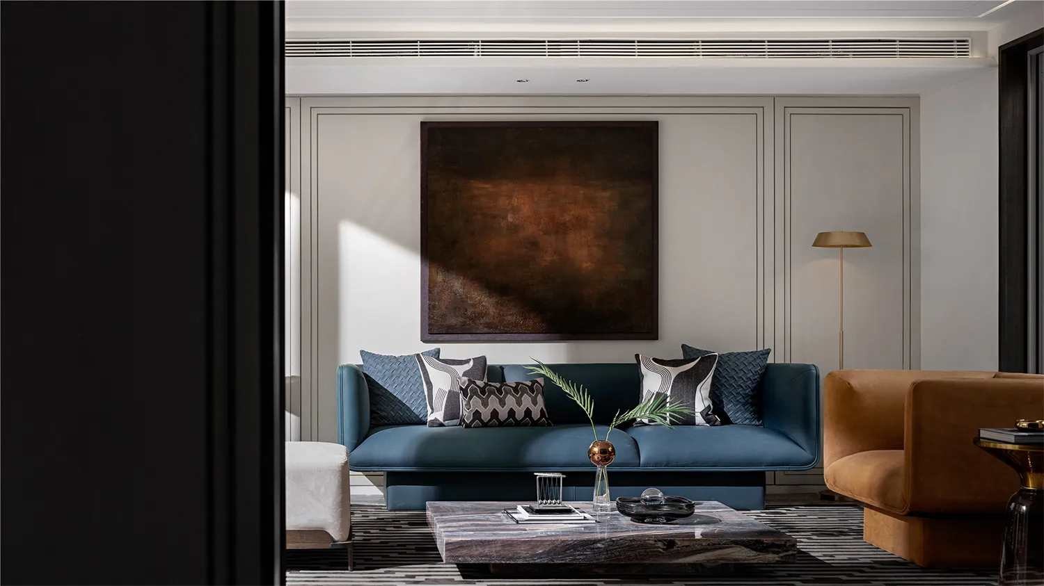 Modern living room with a dark blue leather sofa, marble coffee table, and artistic painting on the wall.