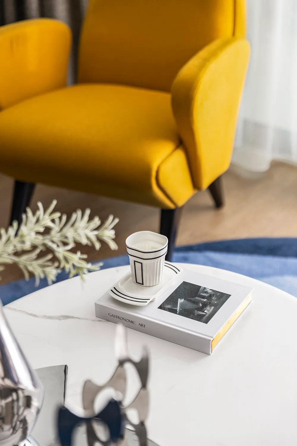 A modern living room featuring a bright yellow upholstered sofa, with a glass coffee table holding a book and a ceramic cup o