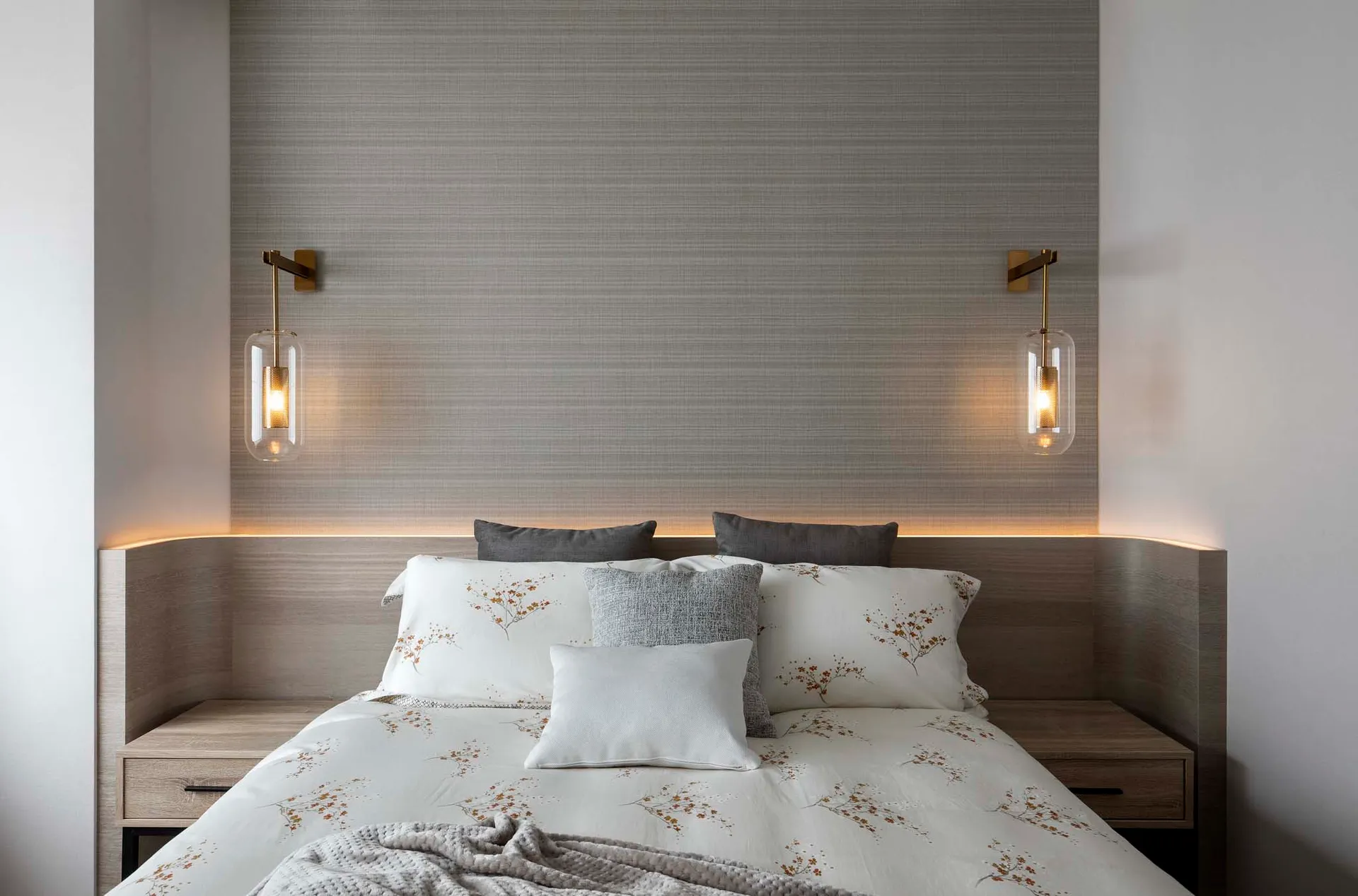 A minimalist bedroom with a bed adorned with floral-patterned bedding, grey pillows, and bedside lamps.