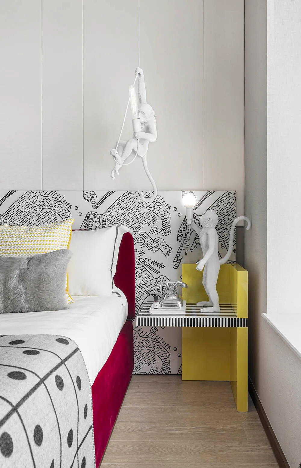 A modern bedroom featuring a monkey-shaped lamp hanging above the bed, with a patterned bedspread and a small bedside table.