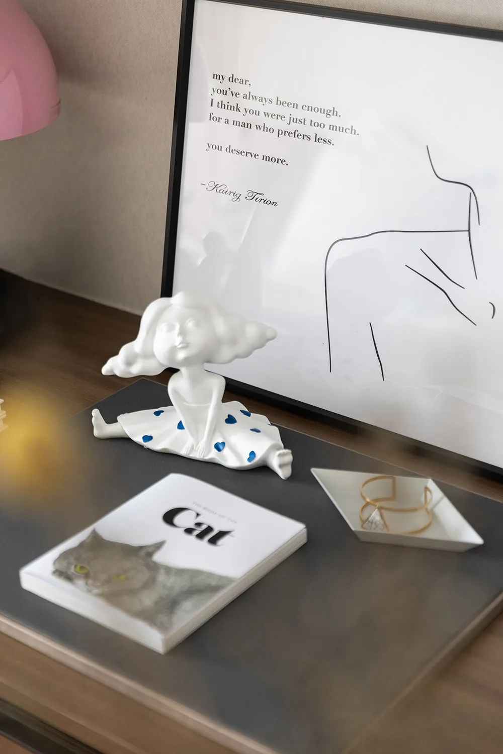 A ceramic figurine of a girl sitting on a book titled 'Cat', with a drawing and text in the background.