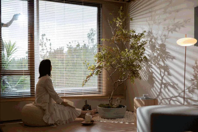 一位女士坐在現代室內客廳的地板坐墊上,周圍擺放植物並有一盞落地燈。
