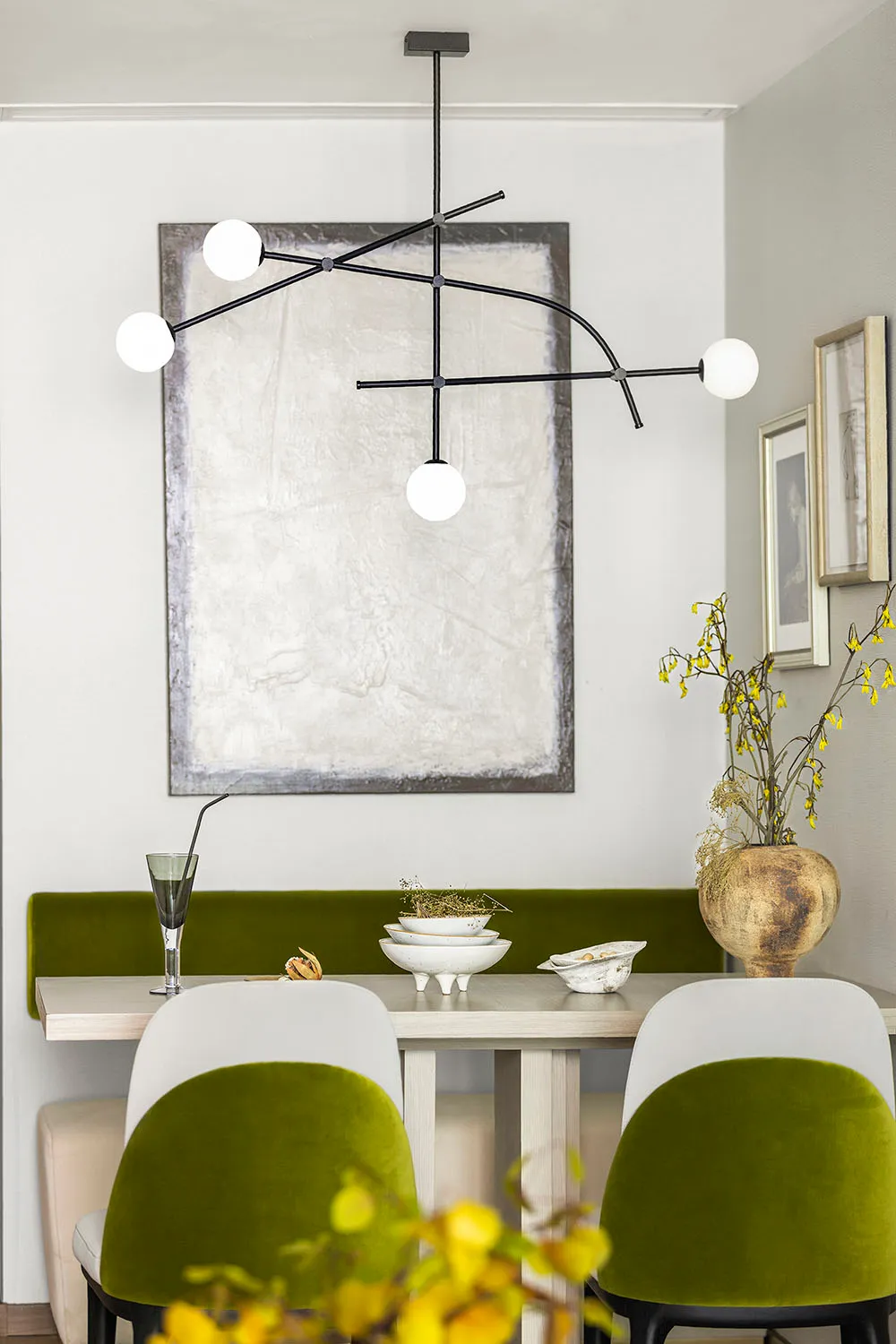 Modern minimalist dining room featuring a sleek metal chandelier, white and green cushioned chairs, and a wooden dining table