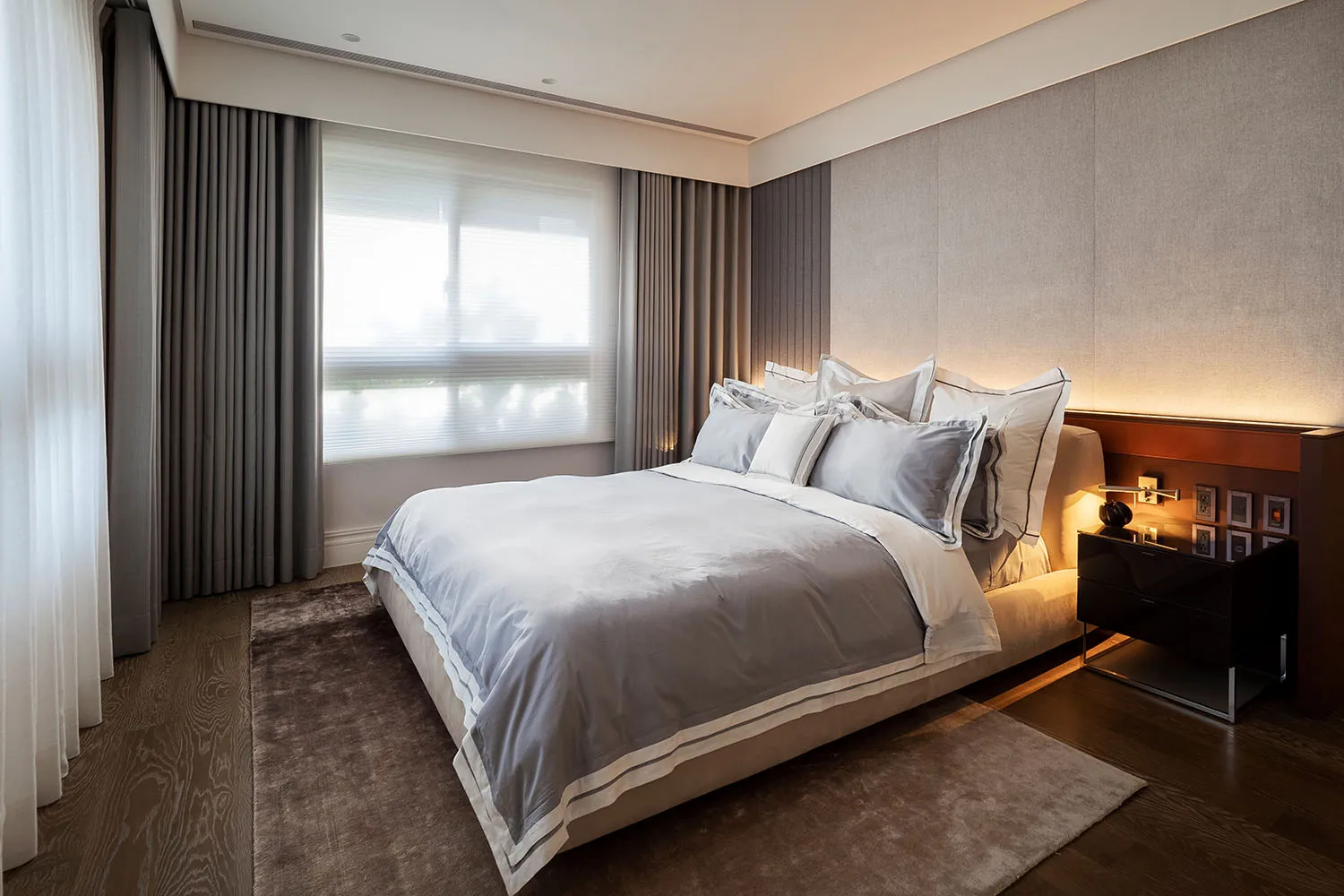 Modern bedroom with fabric bedding, a plush rug, and sleek nightstands.