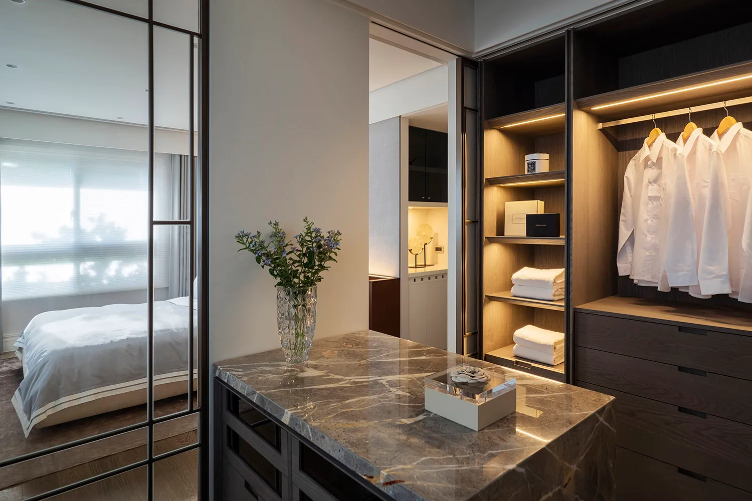 Modern marble closet interior with organized clothing and accessories, featuring a crystal vase with purple flowers, a marble