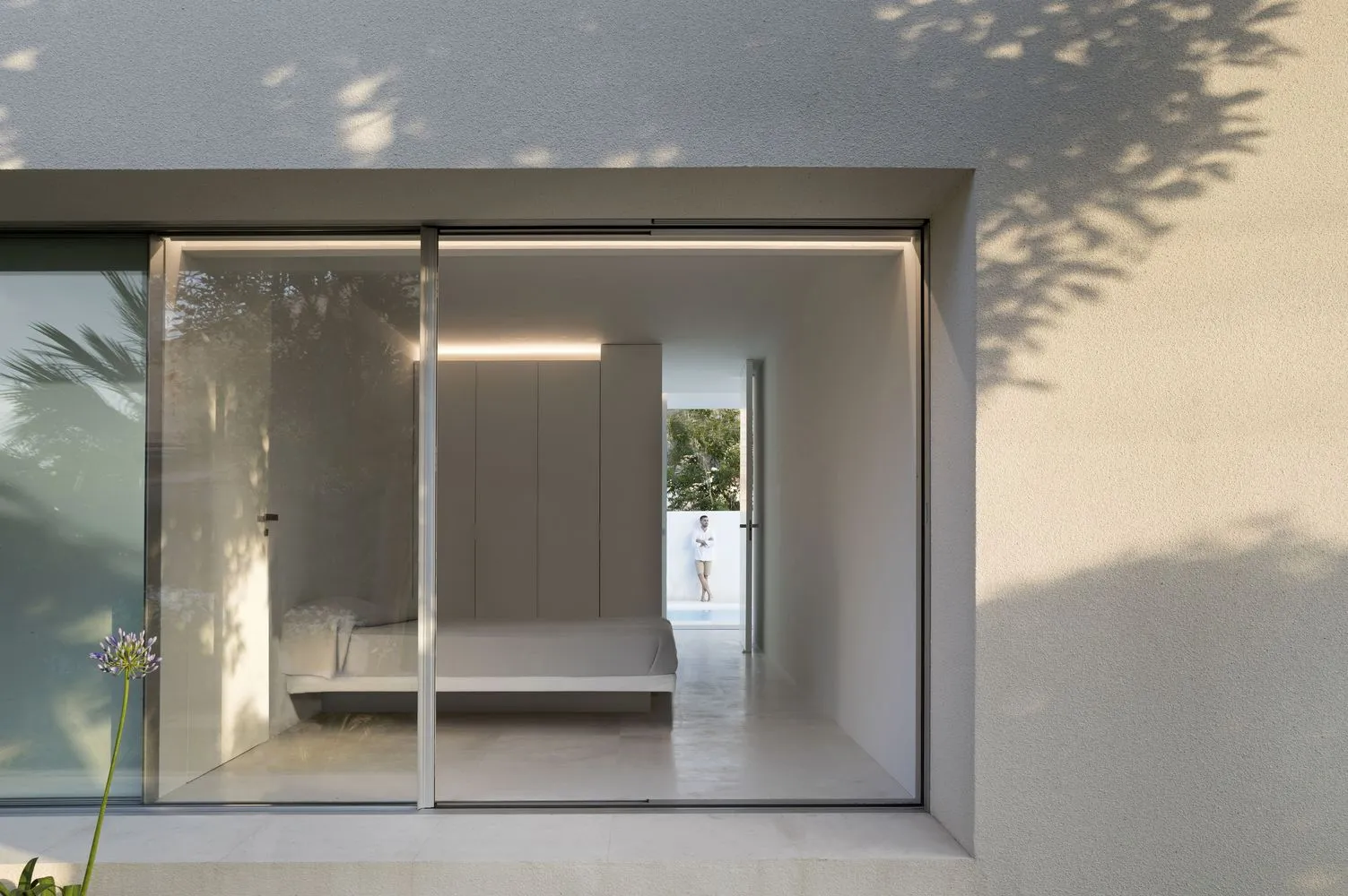 A minimalist bedroom with a concrete floor and walls, featuring a bed and minimal furniture.