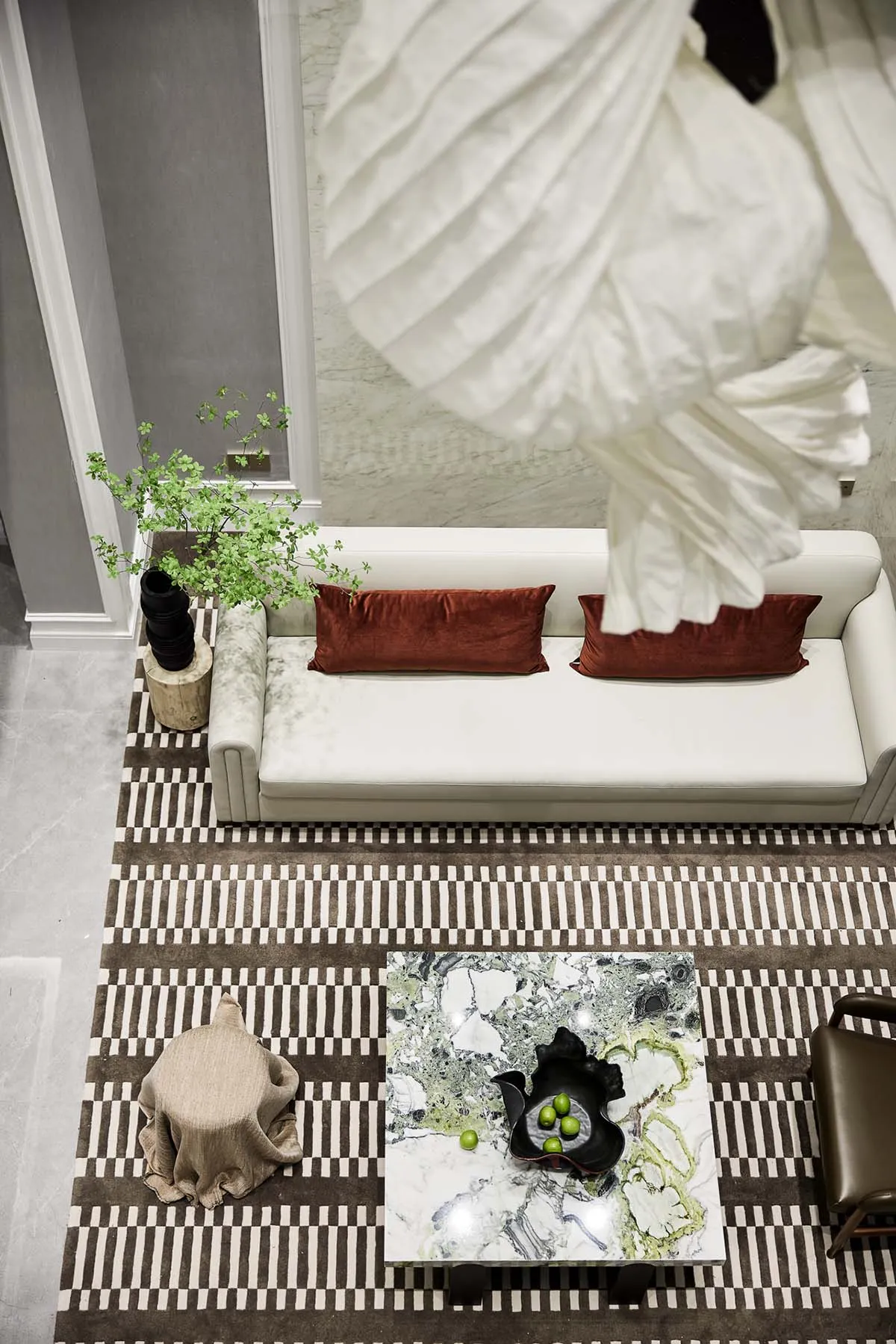 A modern living room featuring a white leather sofa with brown pillows, a marble coffee table, and a patterned rug.