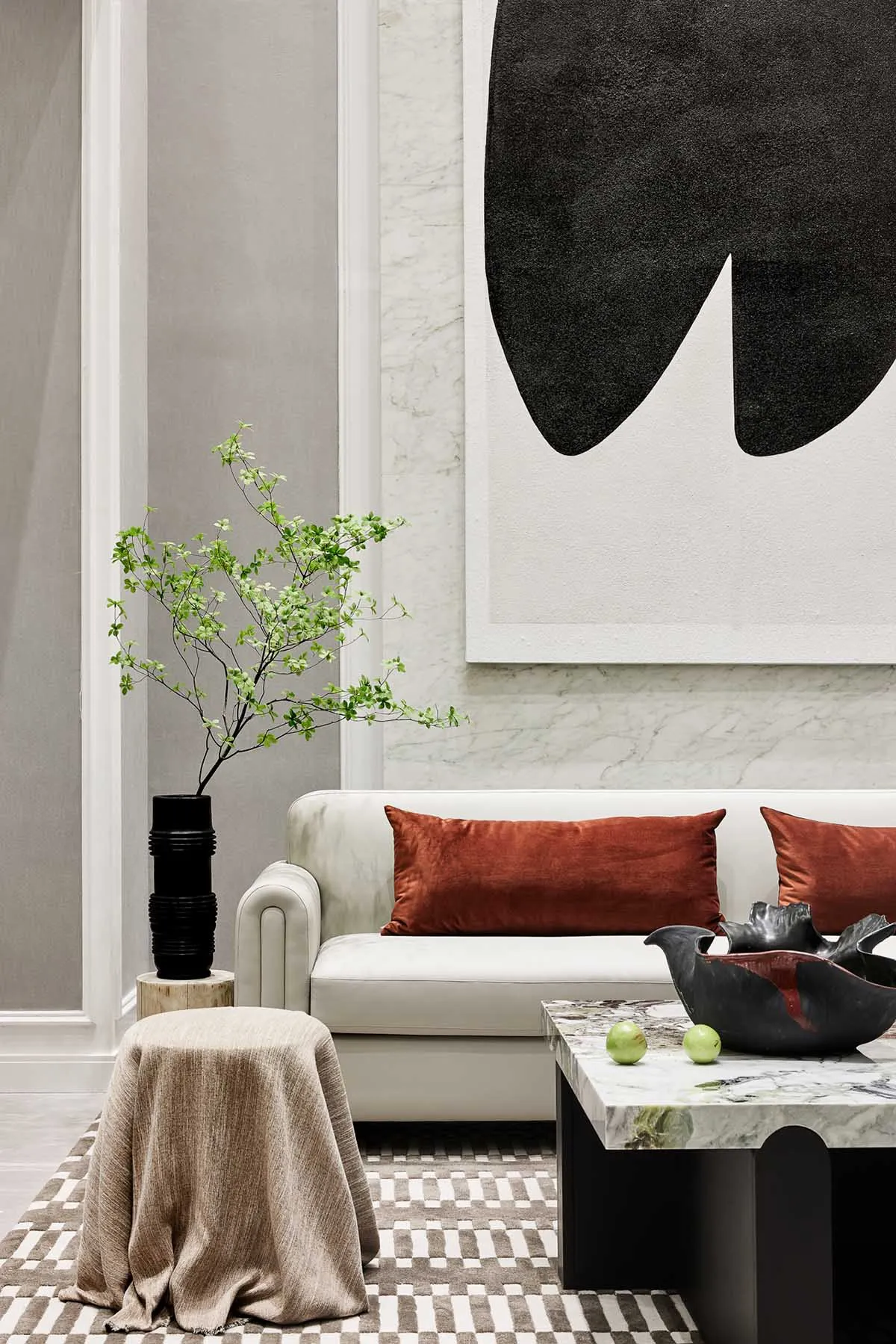 Modern living room with marble coffee table, white sofa with orange cushions, and abstract black and white painting on the wa