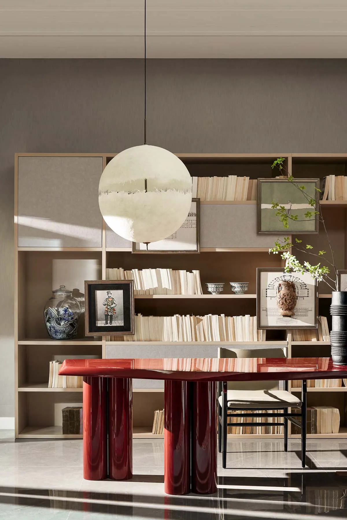 A modern office library with a red lacquered table, books, and hanging light fixture.