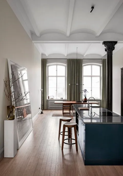 A modern kitchen with dark wood flooring, green curtains, and a dark blue kitchen island.