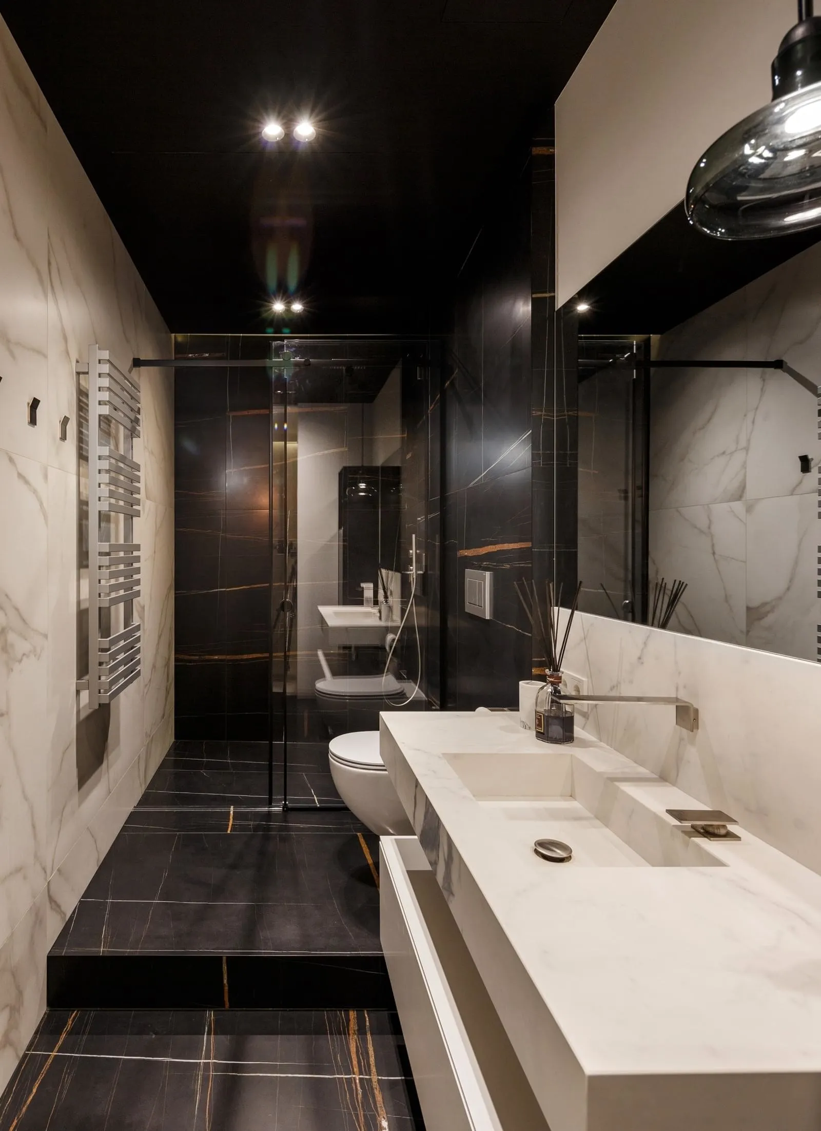 A modern bathroom featuring white marble walls, black marble floor, and a white countertop sink with a black faucet.