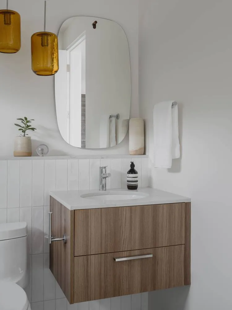 A modern minimalist bathroom with a wooden cabinet, white marble sink, and a framed mirror.