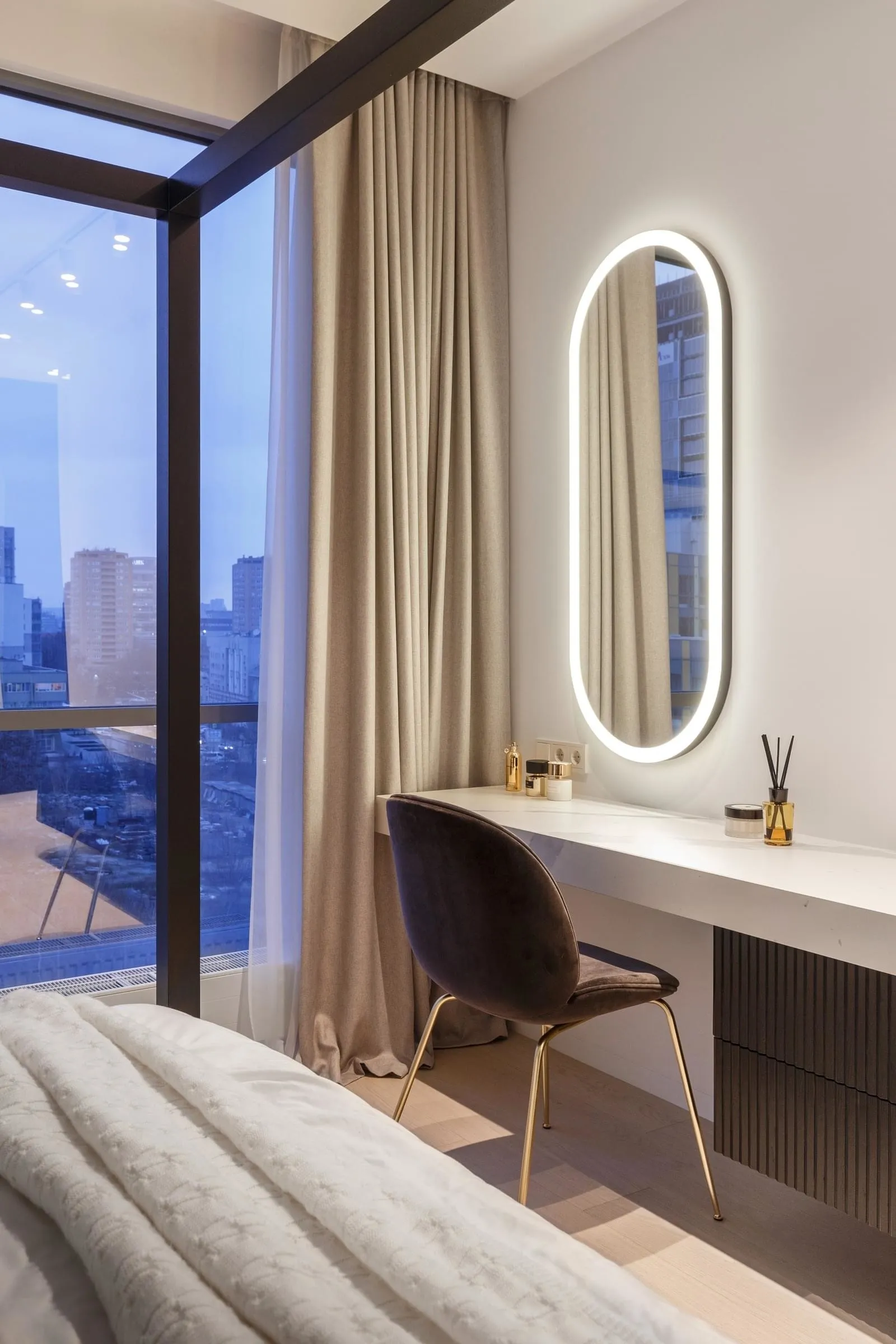 Modern minimalist bedroom with a sleek desk, upholstered chair, and large window overlooking the cityscape.