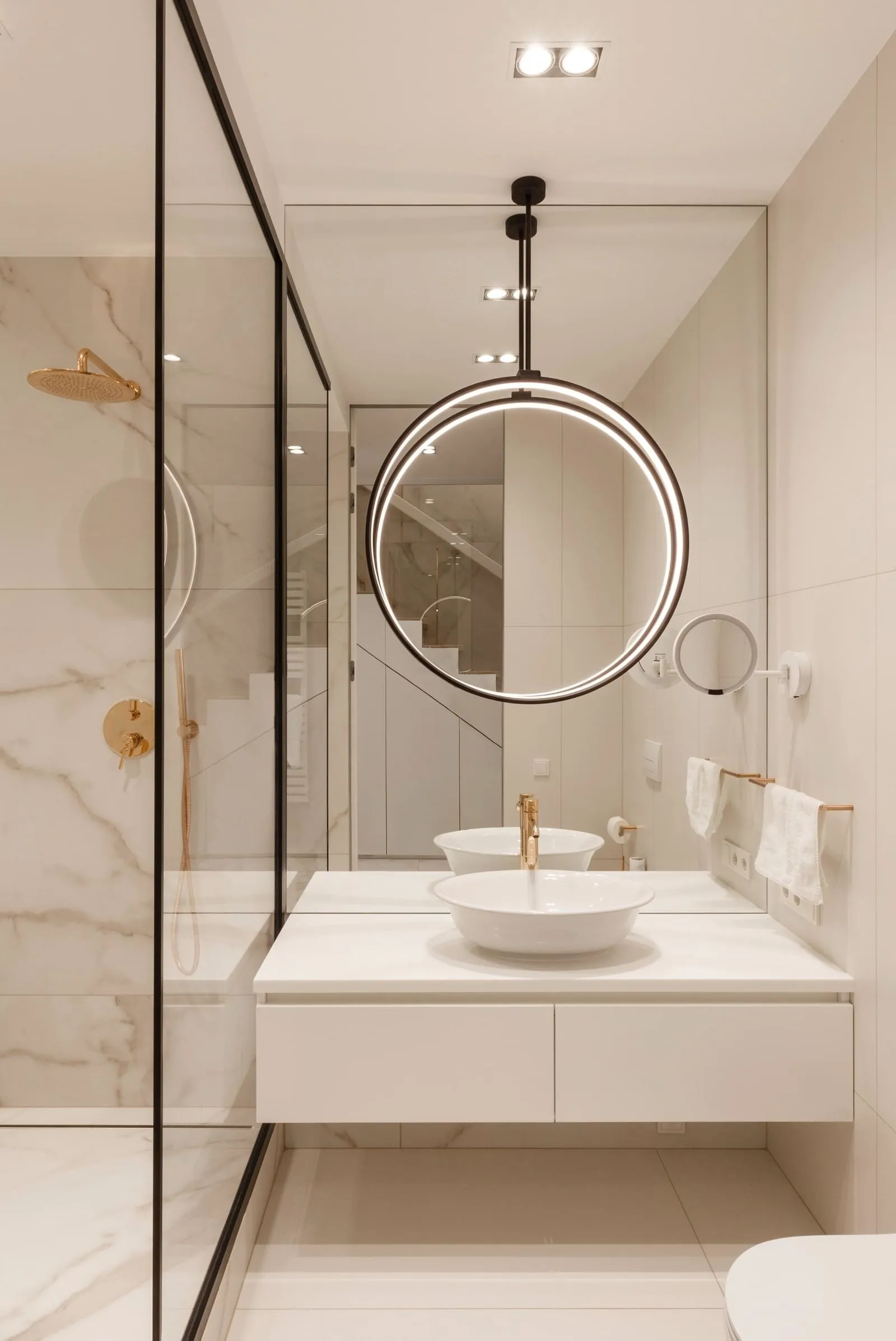 A modern minimalist bathroom with white marble finishes and white porcelain sinks with gold fixtures.