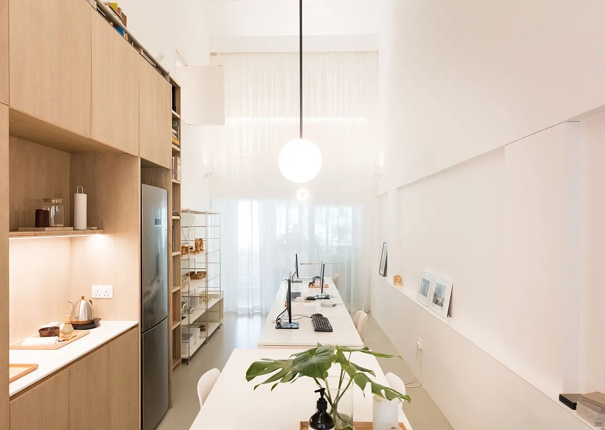 A minimalist residential kitchen with wooden cabinets and a long dining table.