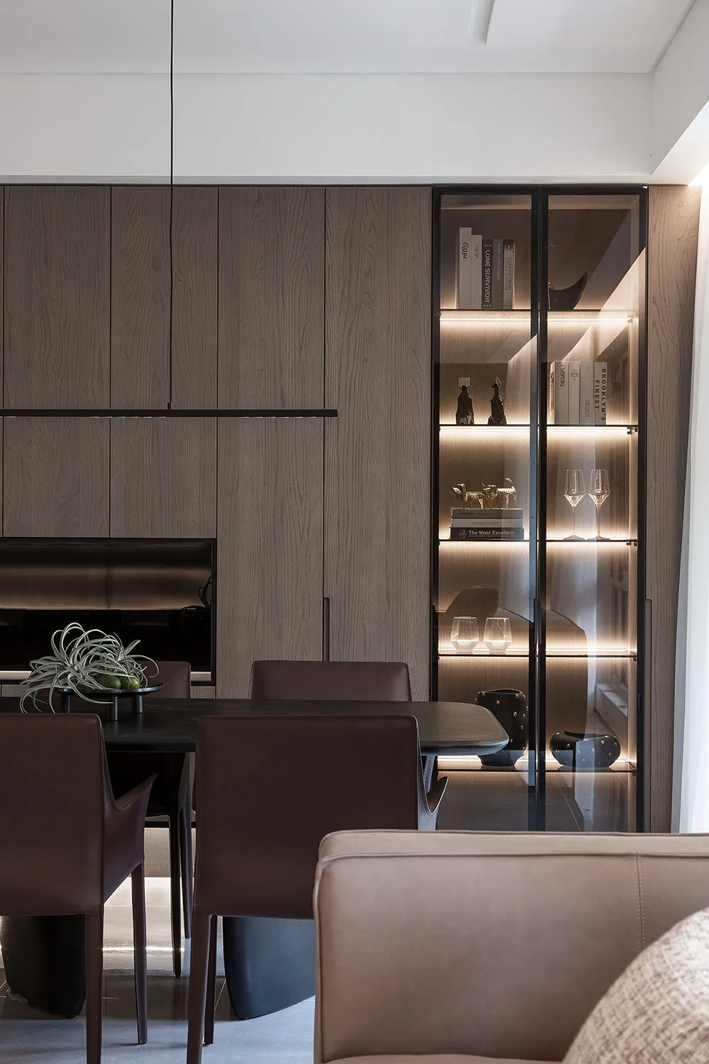 Modern dining room featuring dark wooden table and chairs, glass shelves with illuminated books, and a sleek, minimalist desi