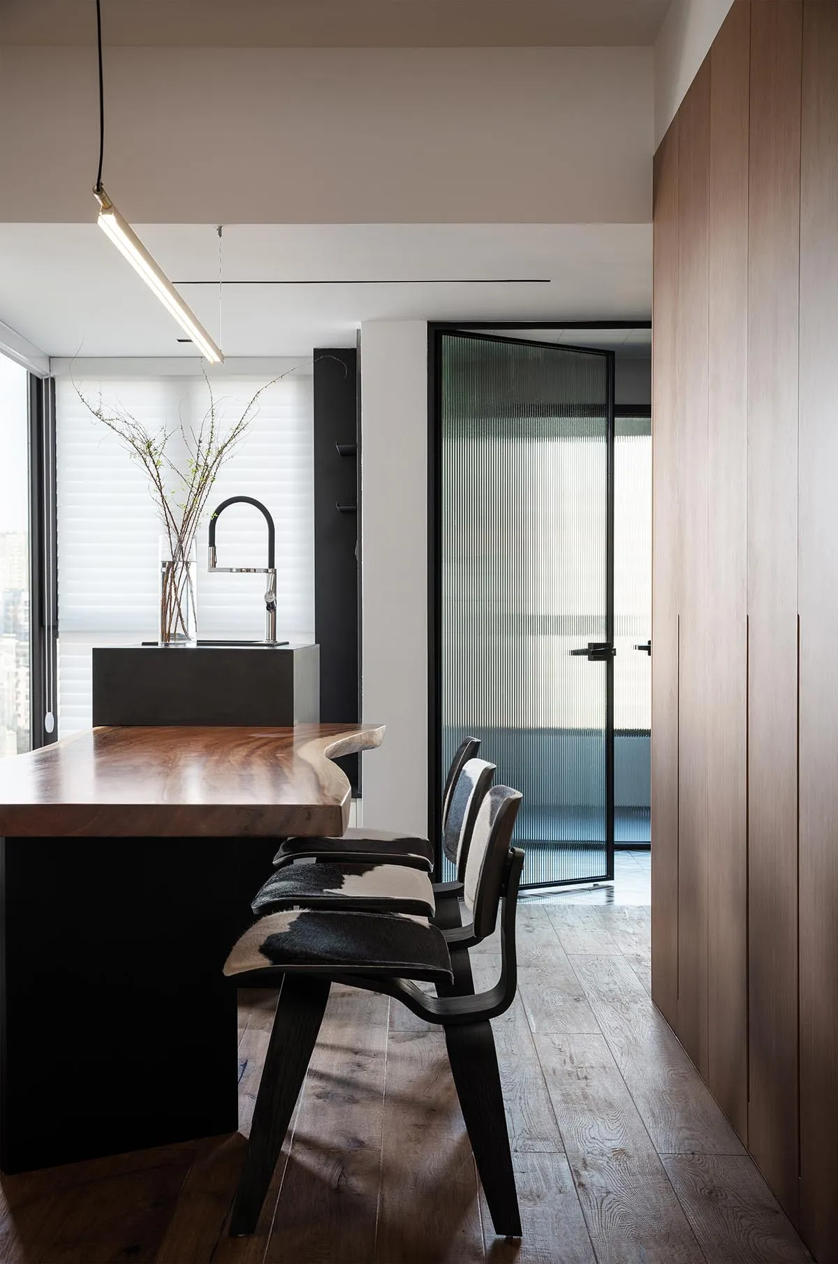 Modern kitchen with wooden counter featuring black and white stools and a sink with a black faucet.