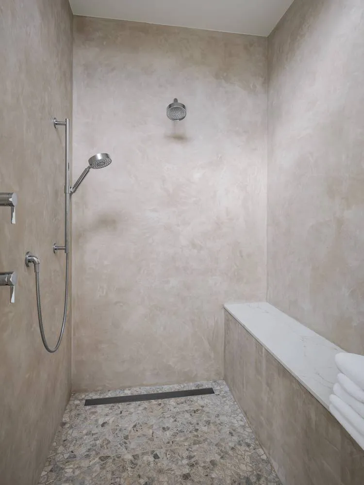 Modern bathroom with concrete walls and minimalist design, featuring a walk-in shower with a bench seat and marble floor tile