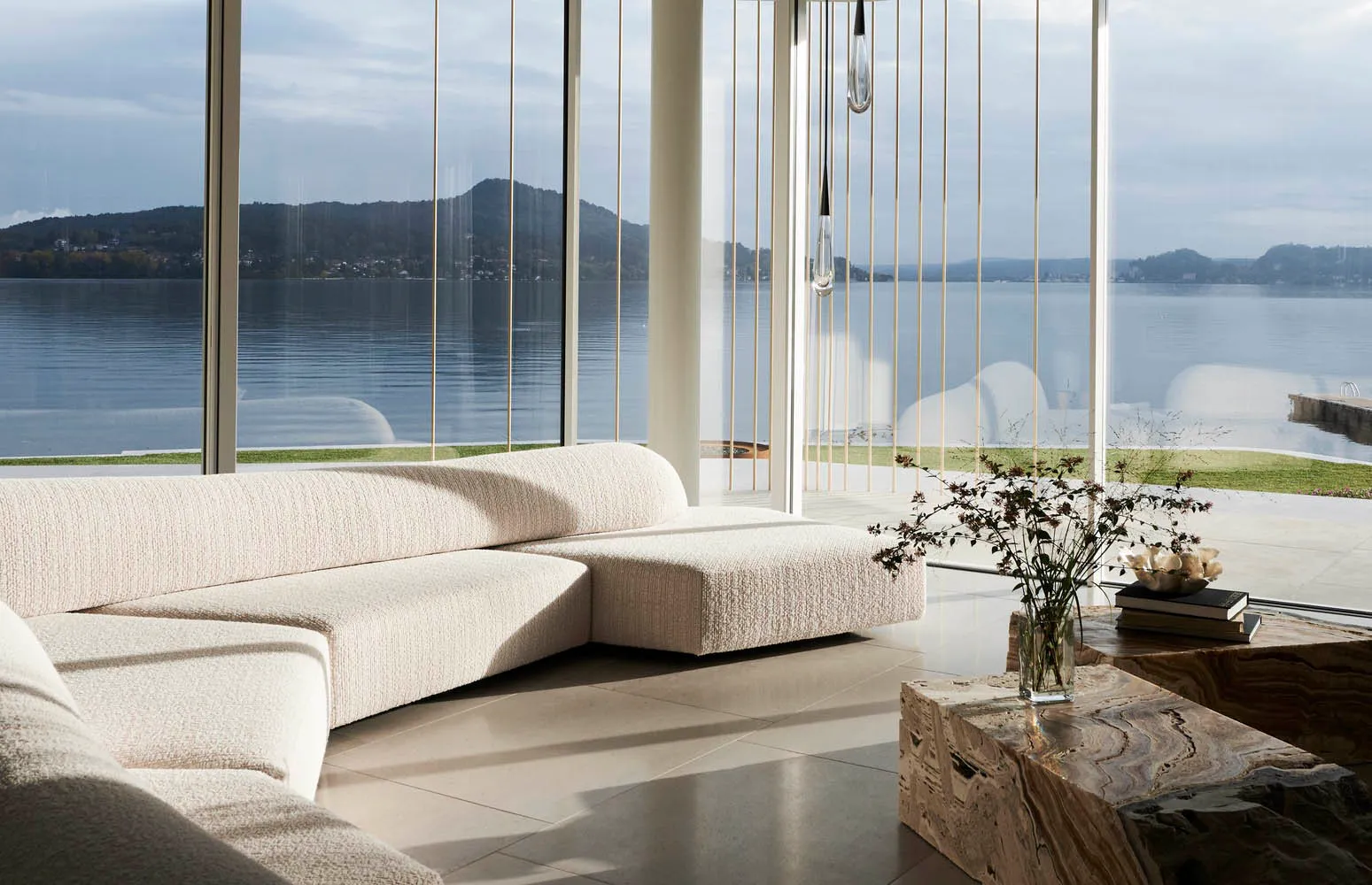 Modern minimalist living room with a white textured fabric couch, large windows overlooking a serene lake view.