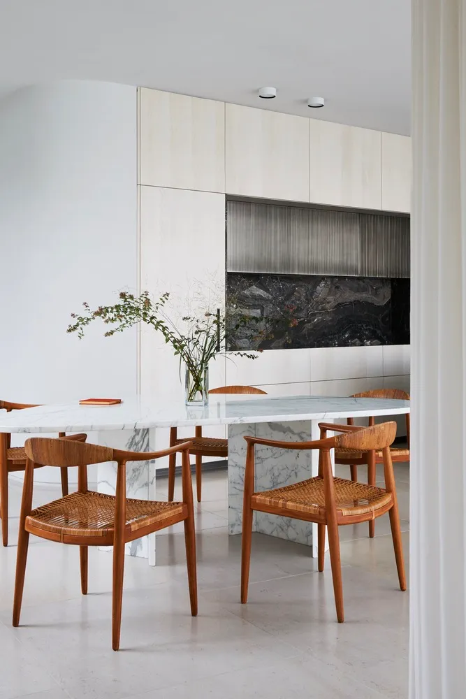 A minimalist dining room with a marble table and wooden chairs.