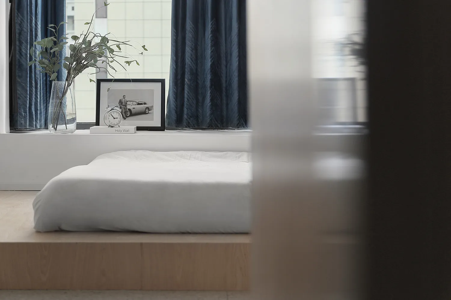 Minimalist bedroom with a wood frame bed, white bedding, and blue curtains.