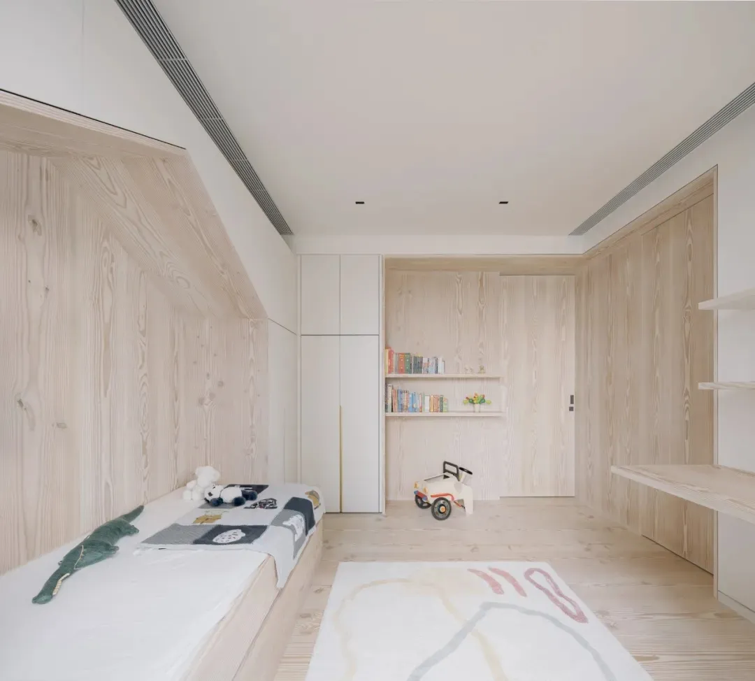 A minimalist children's bedroom with wood paneling, a bed with stuffed animals, and bookshelves.