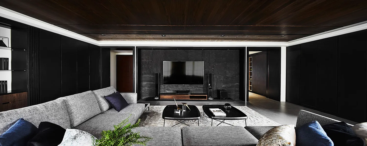 Contemporary living room with grey sofas, black walls, and a large flat-screen TV.