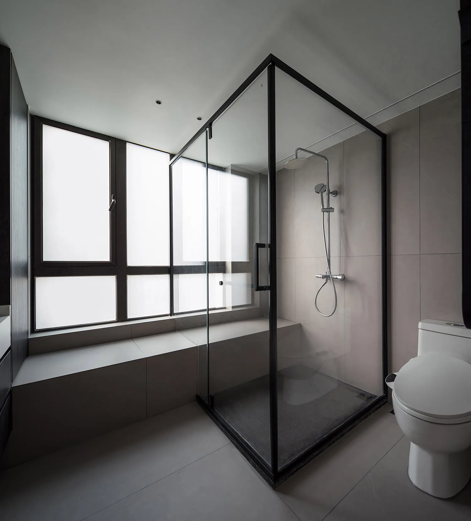 A minimalist modern bathroom with glass shower enclosure, white tiles, and a window seat.