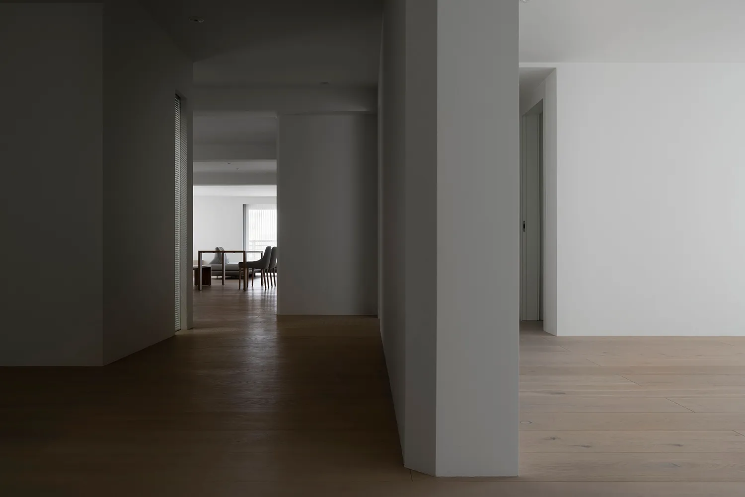 A minimalist apartment with a white interior featuring a living room, dining area, and hallway with wooden flooring and white