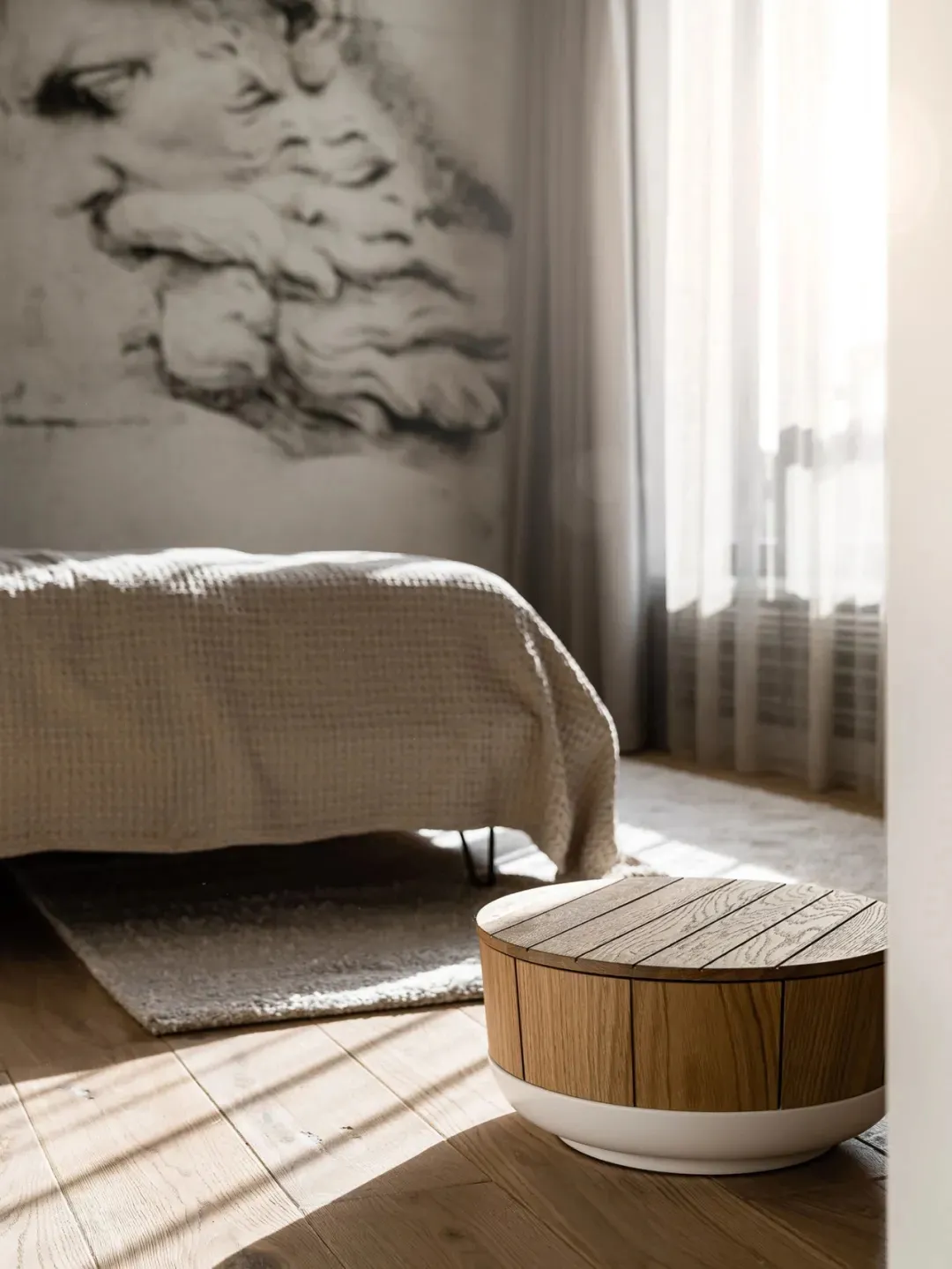Modern minimalist bedroom featuring a white bed and wooden floor with natural light streaming in.