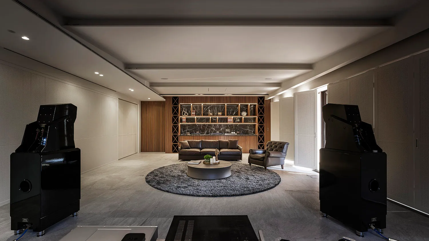Modern living room with concrete floor, leather furniture, marble accents, and wooden shelves.