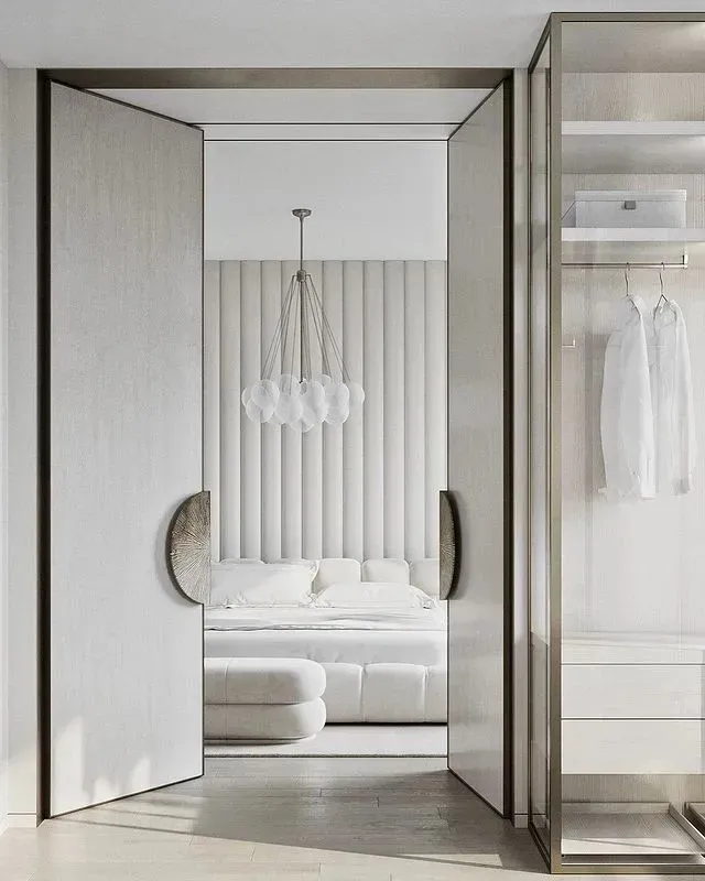 A modern minimalist bedroom with a bed, mattress, and headboard, featuring a chandelier and a closet with white clothing.