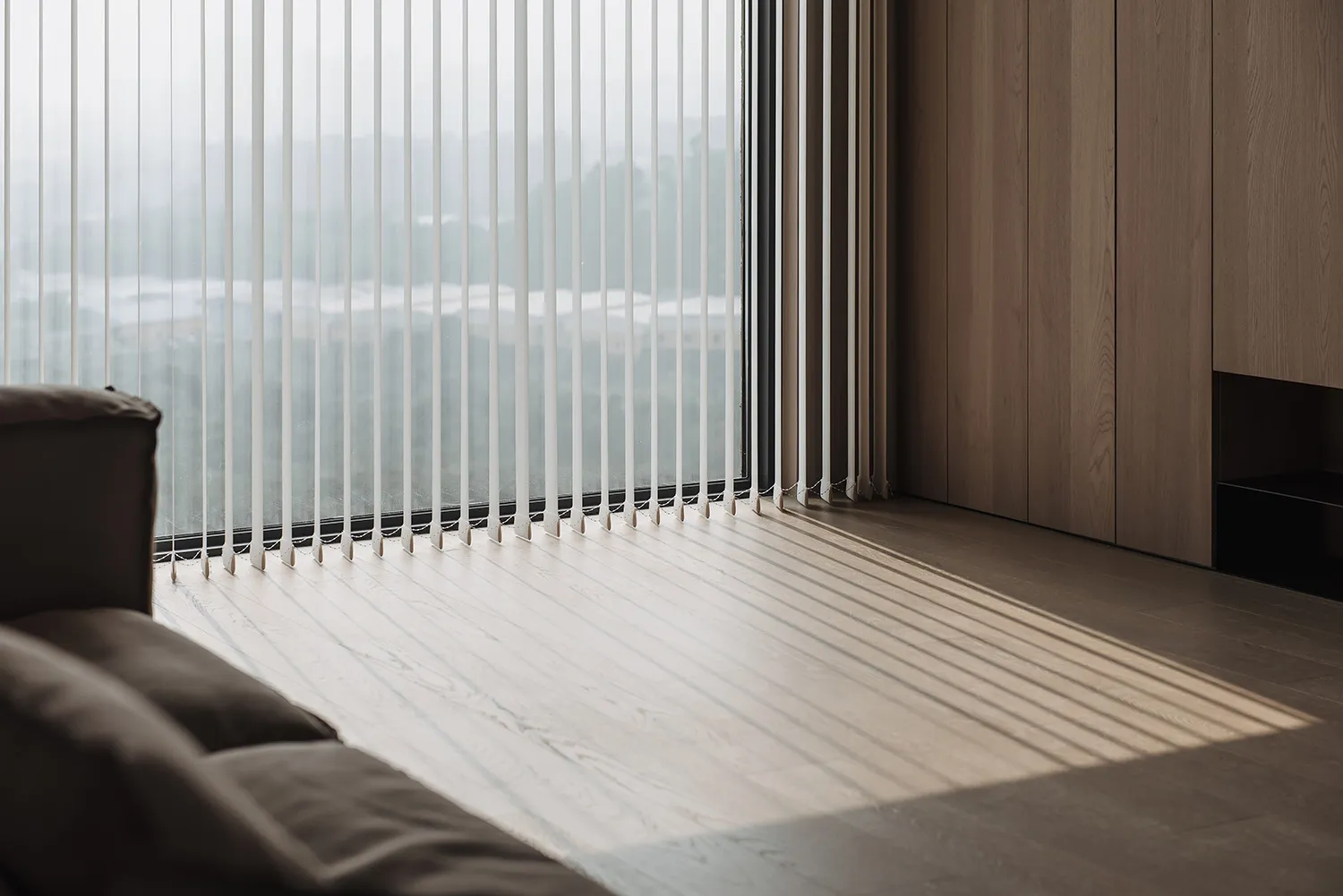 Modern minimalist living room with wooden flooring and vertical blinds.