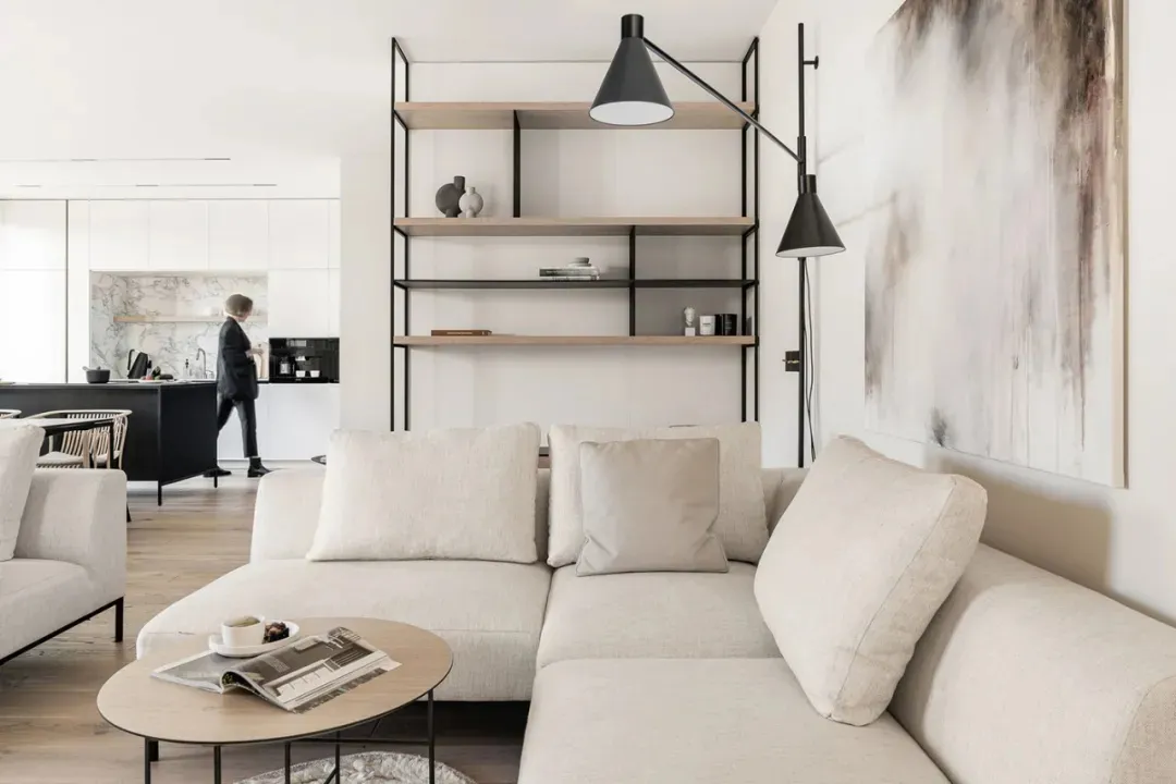 A modern living room featuring a neutral-toned sofa, minimalist shelving, and abstract wall art.
