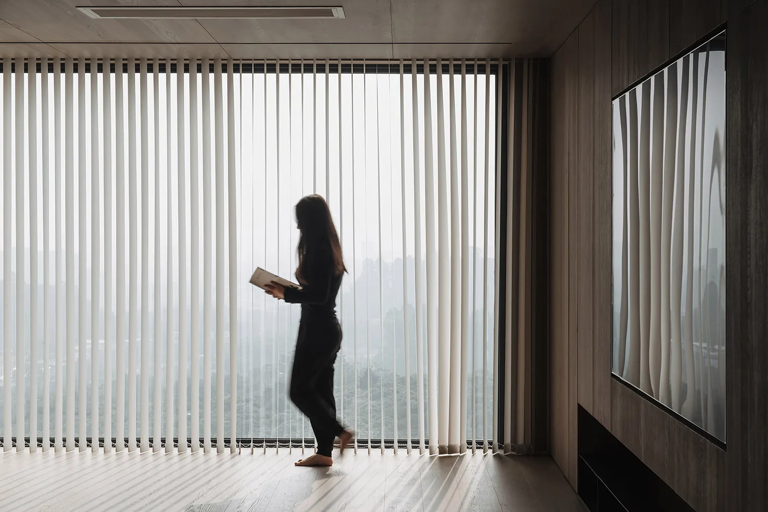 A person walking between vertical blinds with a wooden panel wall