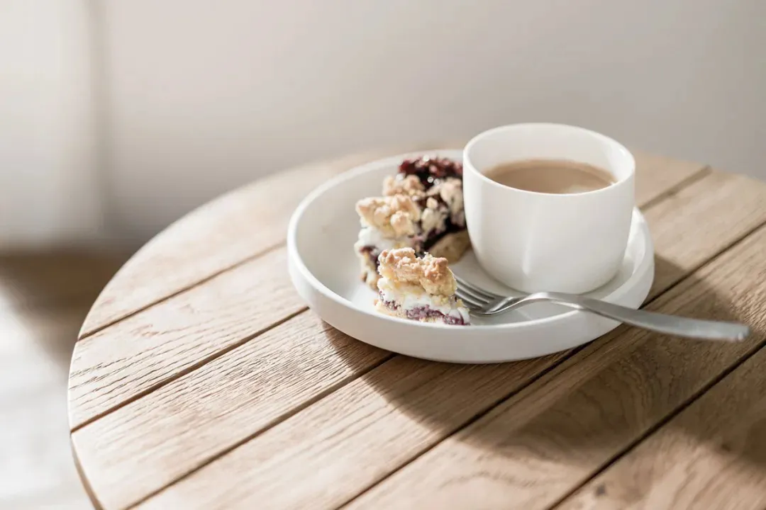 A white cup and plate with food and a fork on a wooden table