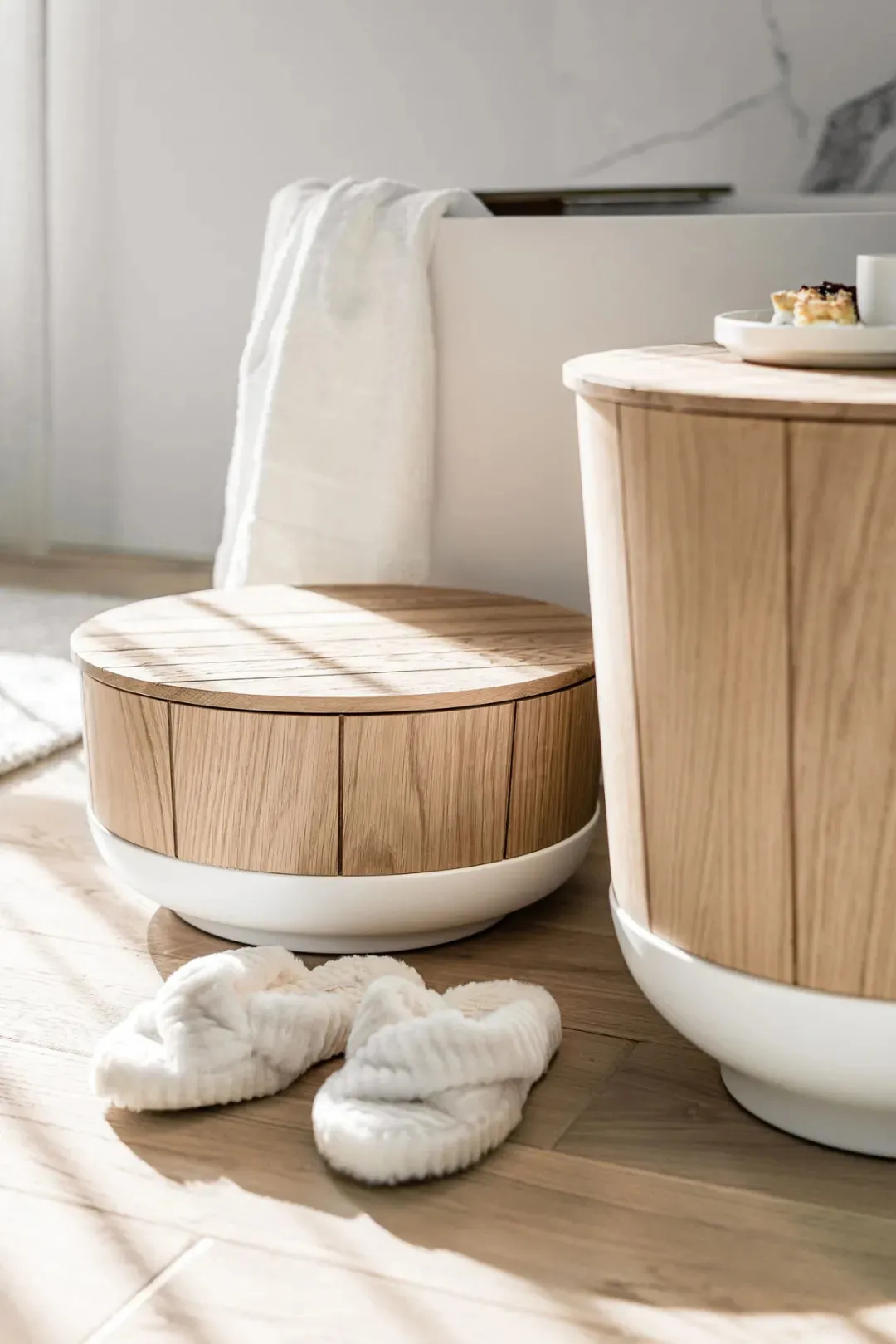 Two minimalist white plastic and wood furniture pieces, one with a round top and the other cylindrical, placed on a light-col