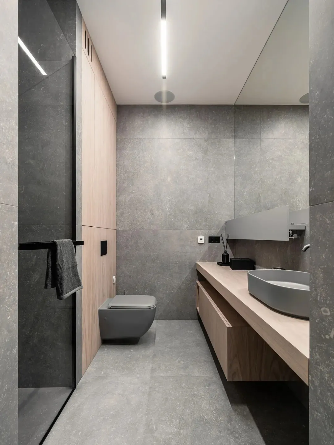 Modern, minimalist bathroom with concrete walls and floor, featuring a floating wooden vanity with a round sink and a closed-