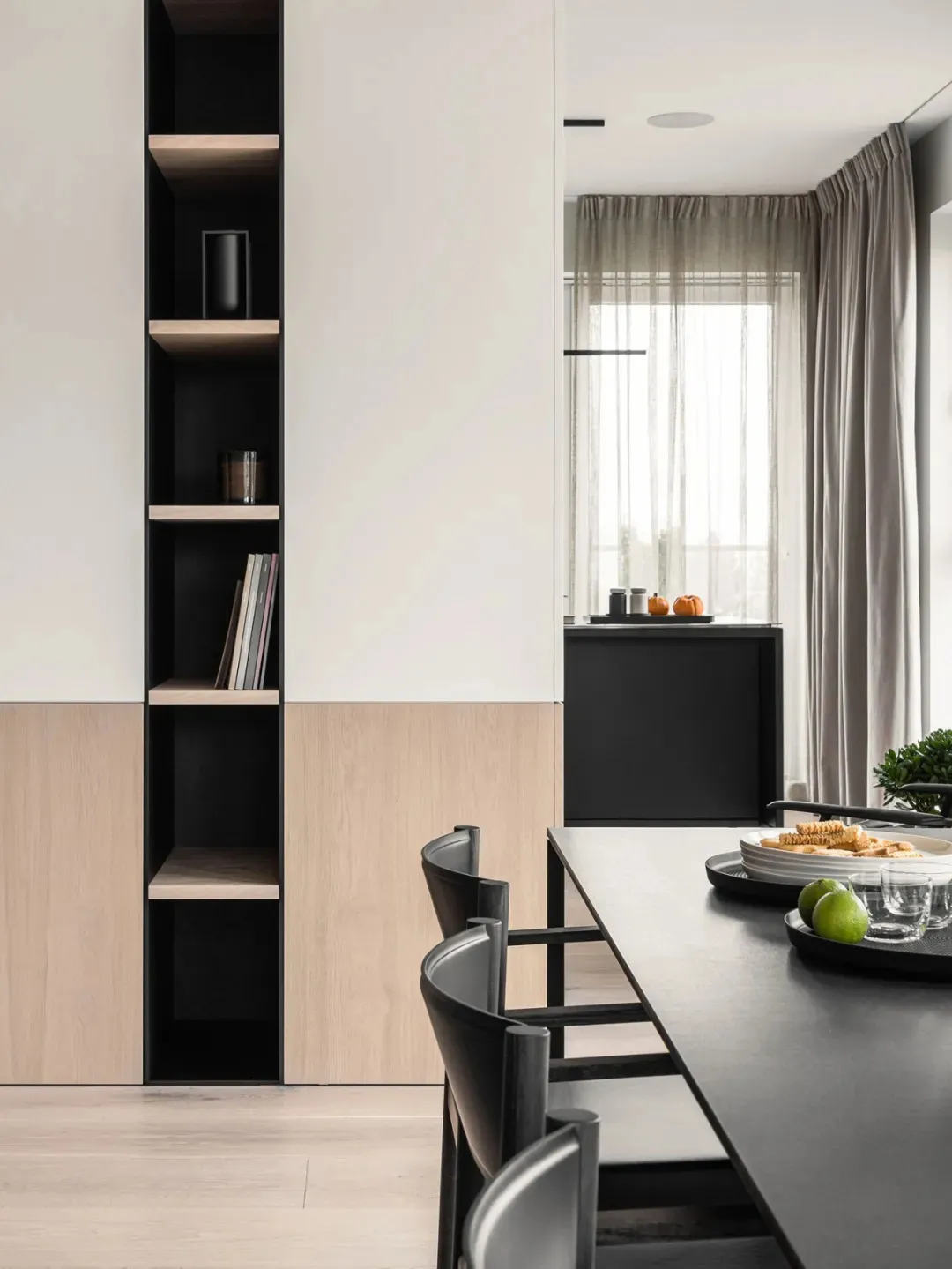 A modern dining room featuring minimalist furniture, sleek black and light wood finishes, and a long black dining table surro