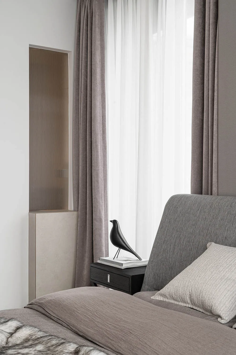 A modern grey bedroom featuring a grey upholstered bed with a bird sculpture on a bedside table.