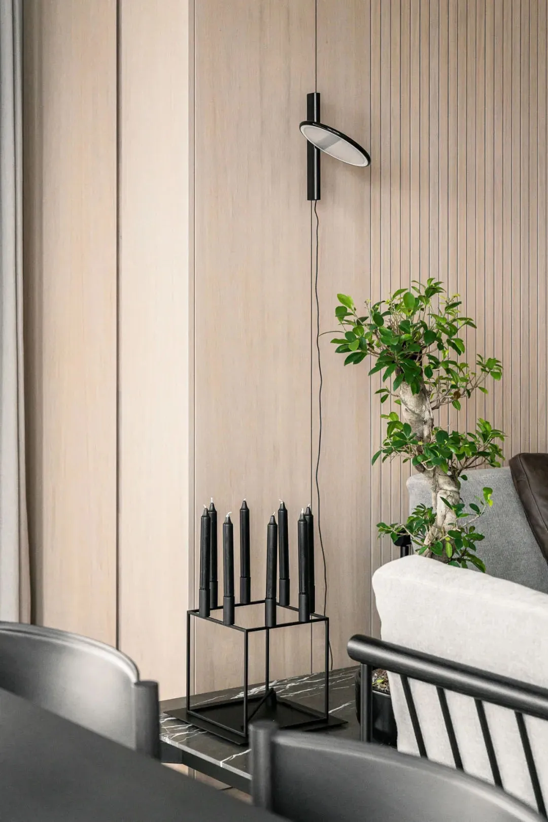 A modern living room featuring a wood-paneled wall, a contemporary floor lamp, a green bonsai tree, and minimalist furniture.