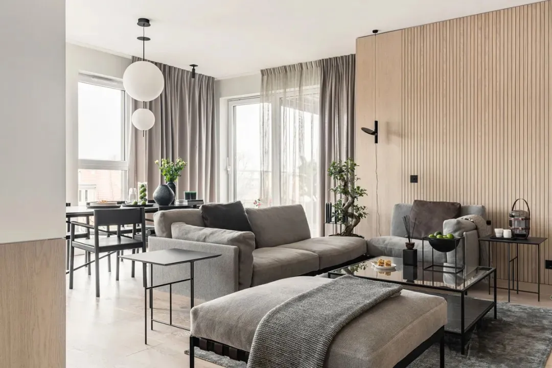 Modern living room with minimalist design, featuring wood paneling, gray furniture, and sleek black accents.